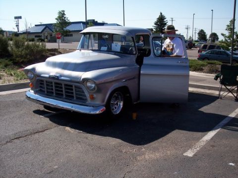 1972 Ford Ranchero - A silver 1955 Chevrolet pickup truck is parked in a lot, with the driver's door open and a man seated inside.