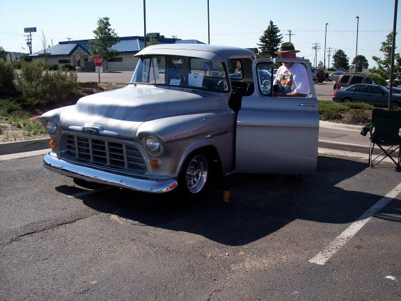 Silver 1955 Chevrolet pickup truck, driver's door open, man in hat visible inside