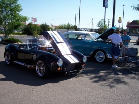 1972 Ford Ranchero - A black convertible with racing stripes is displayed with its hood open, alongside a teal classic car at an outdoor event.