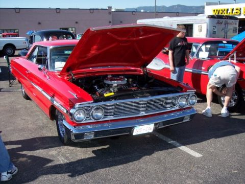 1972 Ford Ranchero - Two classic red cars are parked side-by-side at an outdoor event, with one's hood open to display its engine.