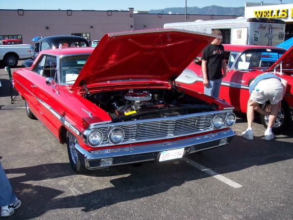 Red classic car, hood open showing engine. Another red classic car next to it. License plate reads 108-CA4