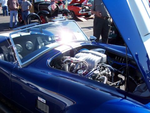 1972 Ford Ranchero - Blue convertible sports car with hood open showing engine. Other cars and people in background.