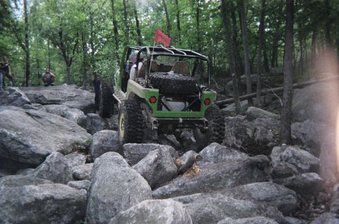 1976 GMC C/K Pickup - A modified jeep tackles a challenging boulder field on a wooded trail.