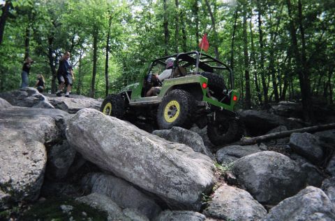 1976 GMC C/K Pickup - A modified off-road vehicle tackles a challenging rocky terrain in a wooded area.