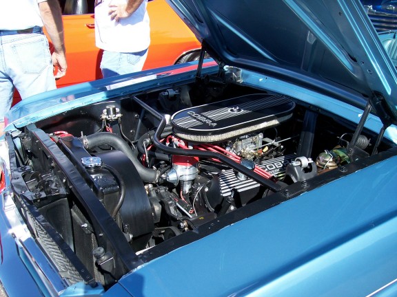 Blue car engine bay with Cobra air cleaner and valve covers. Two people stand behind it
