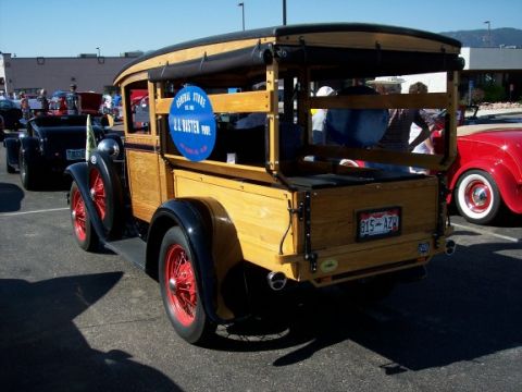 1972 Ford Ranchero - A vintage woodie wagon is parked next to other vehicles, a blue sign on its side.