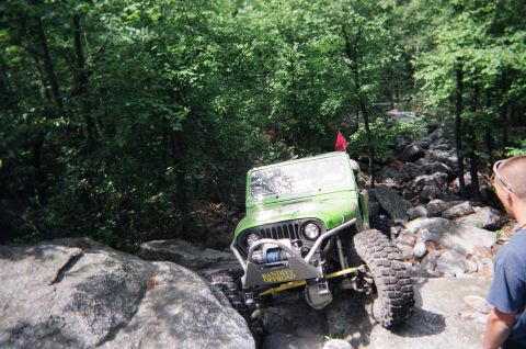 1976 GMC C/K Pickup - Off-road Jeep Wrangler tackling a challenging rocky trail with a red flag on top.