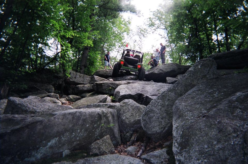 Green off-road vehicle navigating a boulder-strewn path with people watching