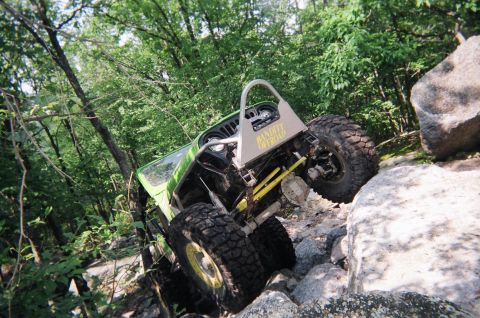 1976 GMC C/K Pickup - This modified Jeep is navigating a difficult rocky terrain on an off-road trail.