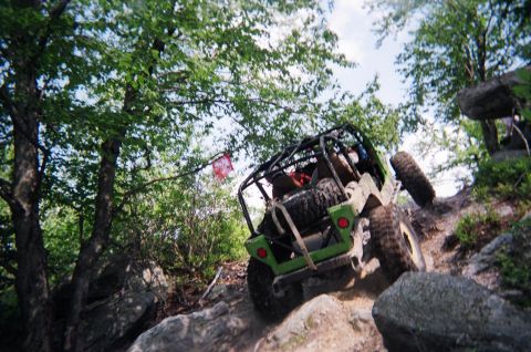 1976 GMC C/K Pickup - Off-road vehicle navigates a rocky incline with trees and boulders surrounding it.