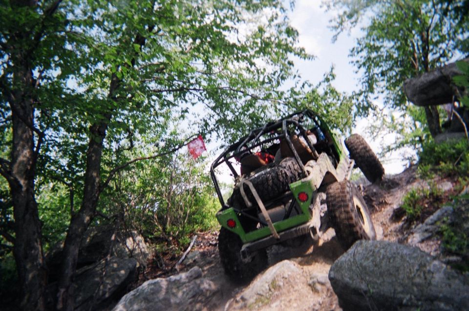 Green off-road vehicle with roll cage climbing rocks, spare tire mounted on rear