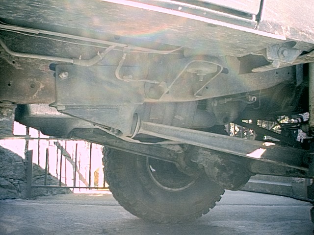 Underbody view of a truck showing front axle, differential, steering linkage, and an off-road tire