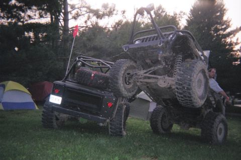 1976 GMC C/K Pickup - Two off-road vehicles are parked near tents, one is lifted up.