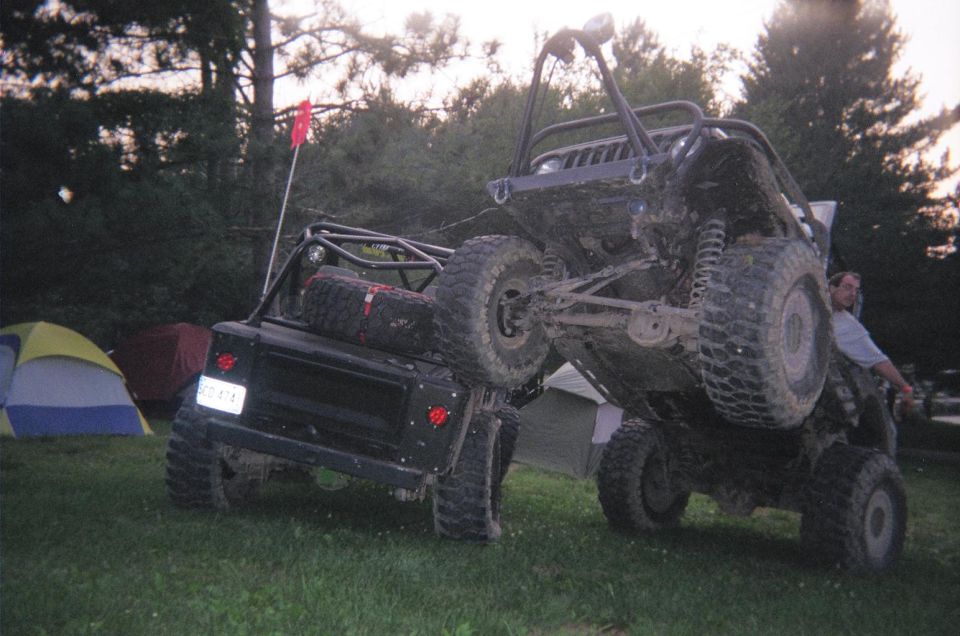 Two off-road vehicles are parked near tents, one is lifted up