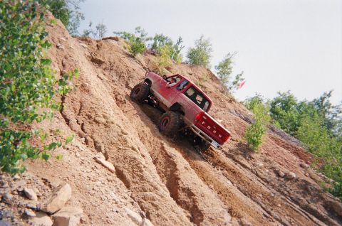 1976 GMC C/K Pickup - A red pickup truck navigates a challenging off-road incline.