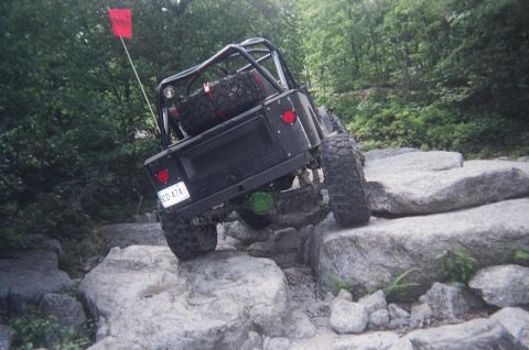 1976 GMC C/K Pickup - Modified Jeep Wrangler tackling a difficult rock crawling course on a wooded trail.