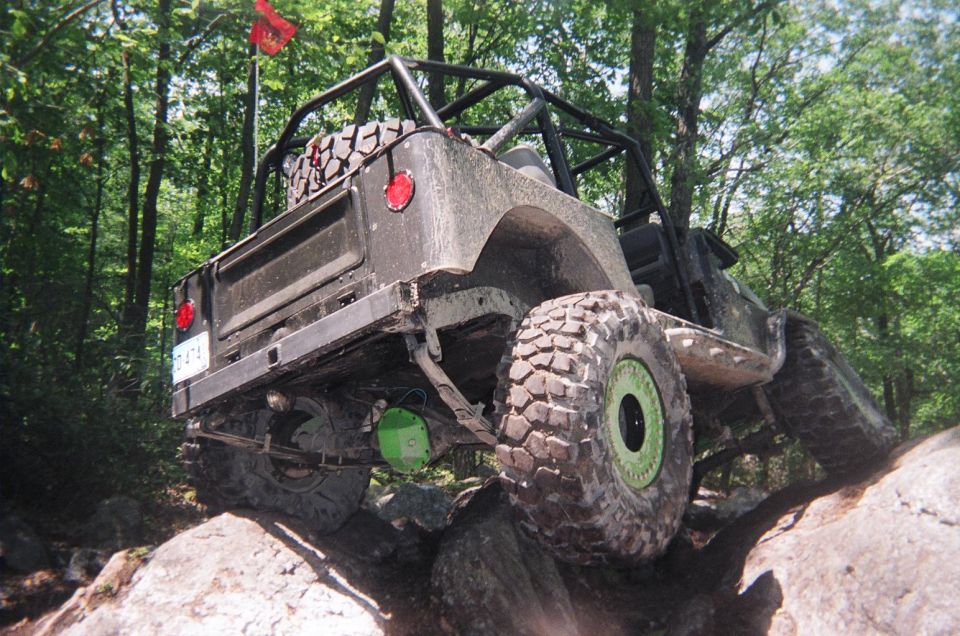 Off-road vehicle with large tires and a roll cage, climbing rocks in a forest