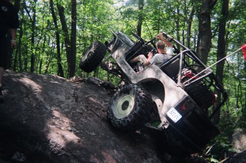 1976 GMC C/K Pickup - An off-road vehicle navigates a challenging rocky terrain in a wooded area.