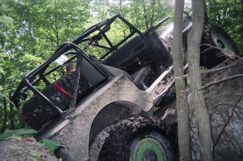 1976 GMC C/K Pickup - An off-road vehicle is stuck sideways between trees and rocks in a wooded area.