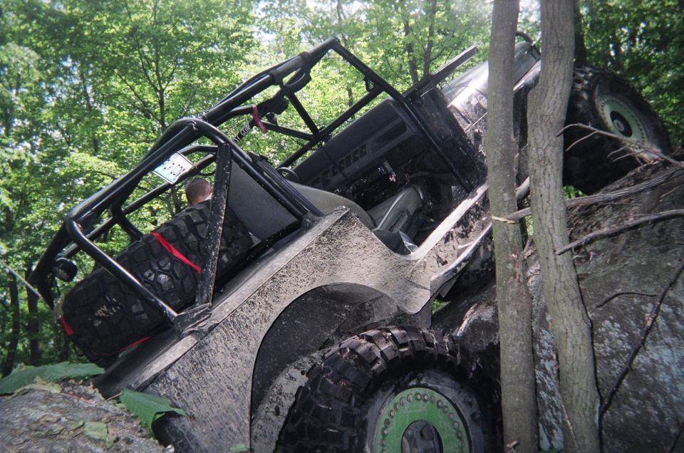 Mud-covered off-road vehicle tilted on its side, wedged between trees and rocks