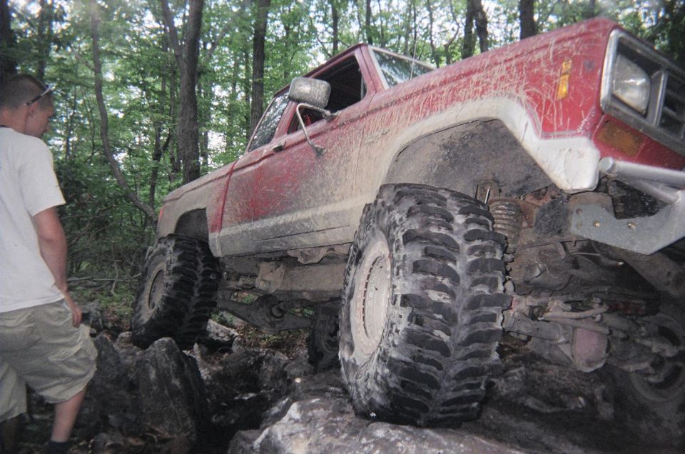 Red off-road truck with large tires navigating rocks, person watching