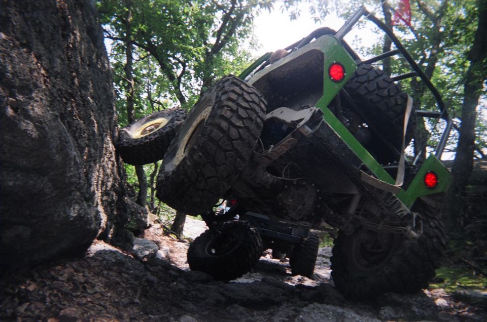 Off-road buggy with large tires climbing over a rock obstacle, another vehicle visible behind it
