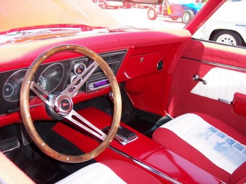 1972 Ford Ranchero - The interior of a red car is visible, with a wood-rimmed steering wheel and a pamphlet on the seat.