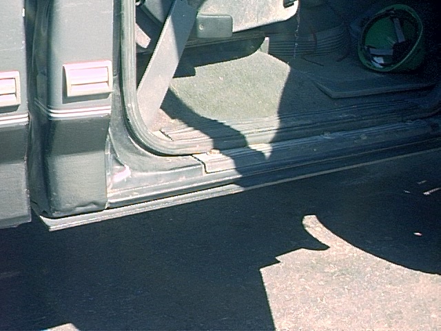 Close-up of open door sill and rocker panel on a dark truck, showing weatherstrip, carpet, and seatbelt