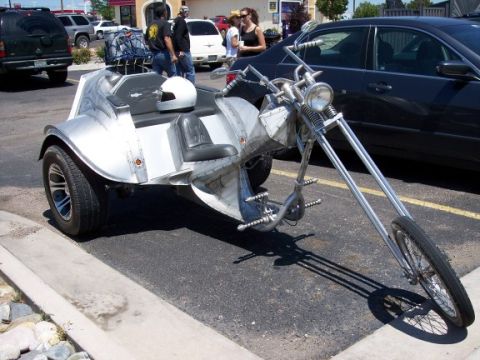 1972 Ford Ranchero - A custom-built trike motorcycle with a distinctive silver body and extended front fork is parked in a lot.