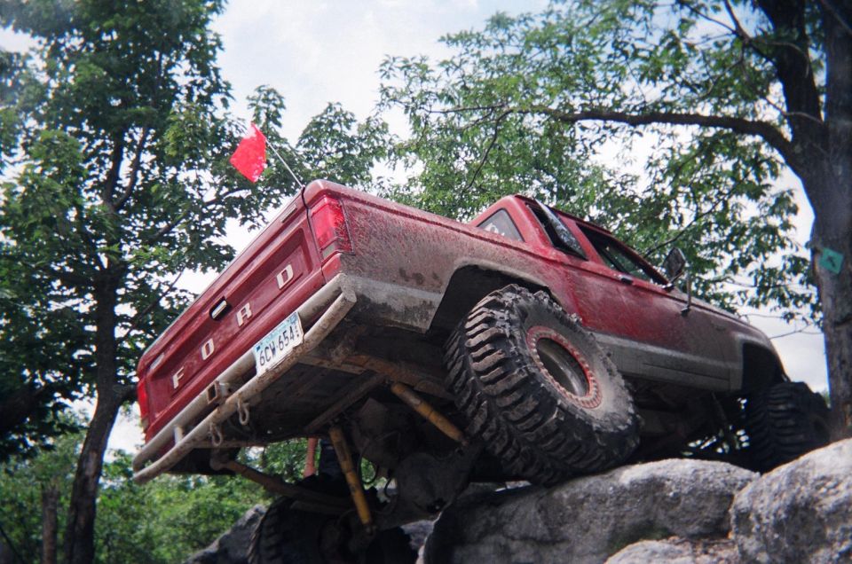 Red Ford pickup truck with large off-road tires climbing over rocks, red flag on antenna