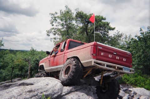 1976 GMC C/K Pickup - This modified Ford pickup is navigating a rocky off-road course with a driver inside.