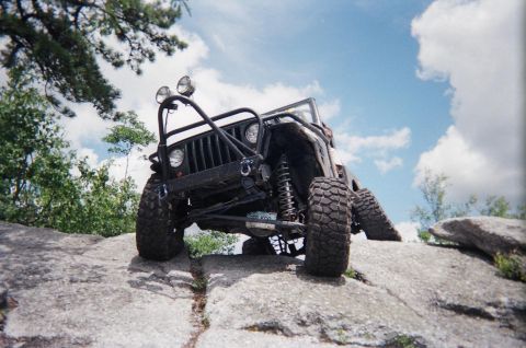 1976 GMC C/K Pickup - A modified Jeep Wrangler navigates a rocky terrain under a partly cloudy sky.