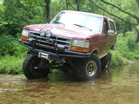 1993 Ford Bronco - This modified 1993 Ford Bronco navigates a shallow stream surrounded by lush green foliage.