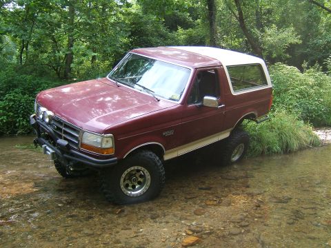 1993 Ford Bronco - 1993 Ford Bronco navigating a stream with trees and foliage in the background.
