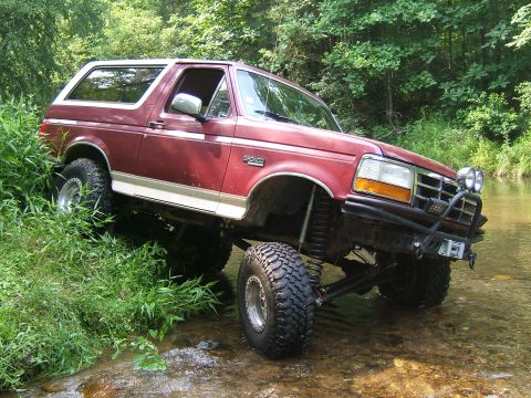1993 Ford Bronco - This lifted Ford Bronco navigates a rocky stream bed surrounded by lush green foliage.