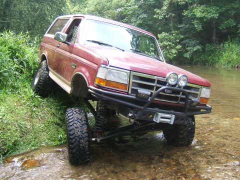 1993 Ford Bronco - A red Ford Bronco navigates a stream with its front tires angled towards the camera.