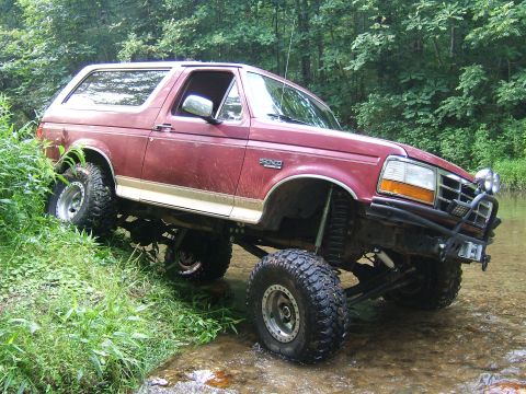 1993 Ford Bronco - This lifted 1993 Ford Bronco navigates a rocky stream bed surrounded by lush green foliage.