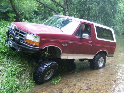 1993 Ford Bronco - This lifted 1993 Ford Bronco navigates a shallow stream surrounded by lush green foliage.