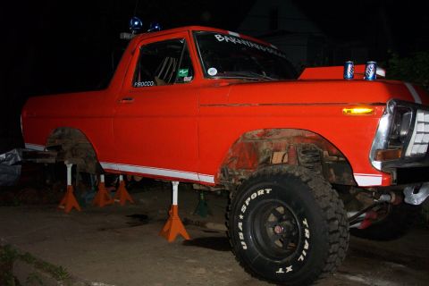 1978 Ford Bronco - This orange truck is on jack stands with its hood up, showing off its off-road tires and custom details.