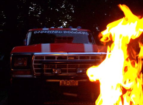 1978 Ford Bronco - A red truck with white stripes and a hood scoop is partially obscured by flames.