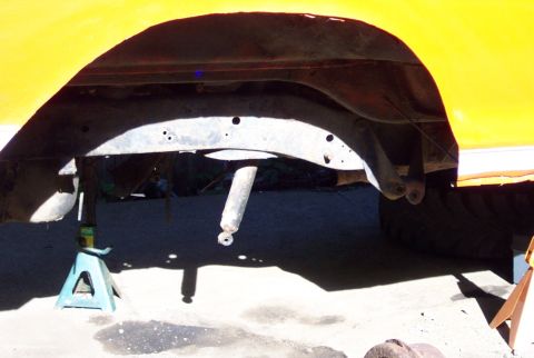 1978 Ford Bronco - The underside of a vehicle is shown, with the frame and suspension components exposed and supported by jack stands.
