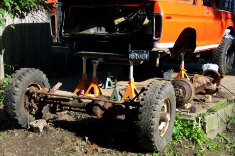 1978 Ford Bronco - The rear axle of an orange SUV is removed and the vehicle is supported by jack stands.