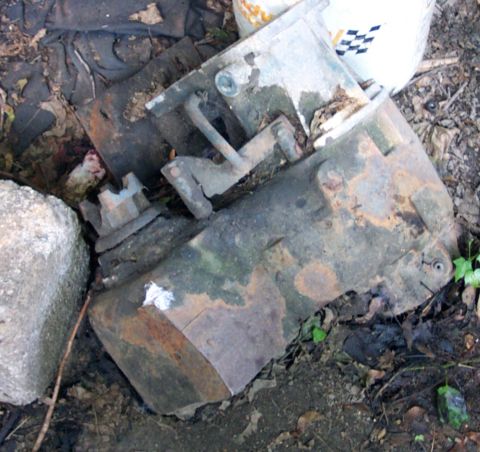 1978 Ford Bronco - This appears to be a heavily rusted engine component lying on the ground amidst debris.