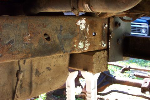 1978 Ford Bronco - The underside of a vehicle's frame shows significant rust and is supported by a wooden block.