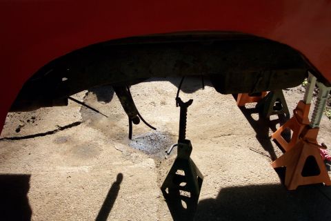 1978 Ford Bronco - The undercarriage of a red vehicle is supported by jack stands, revealing its frame and suspension parts.