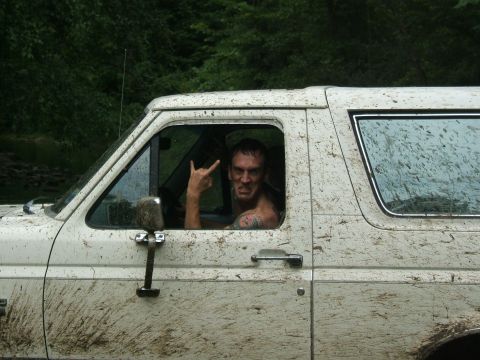 1993 Ford Bronco - Man in a very muddy white 1992 Ford Bronco makes a rock horns hand gesture.