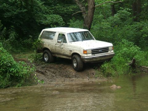 1993 Ford Bronco - A white 1993 Ford Bronco navigates a muddy trail next to a body of water.