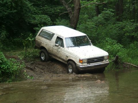 1993 Ford Bronco - White Ford Bronco navigating a muddy stream in a wooded area.