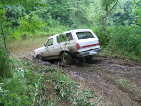 1993 Ford Bronco - A white 1993 Ford Bronco navigates a muddy trail, partially submerged in water.