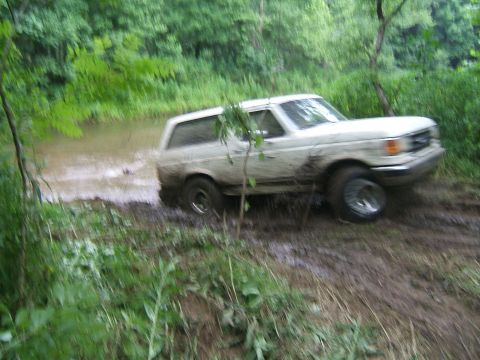 1993 Ford Bronco - White Ford Bronco navigating a muddy off-road trail.